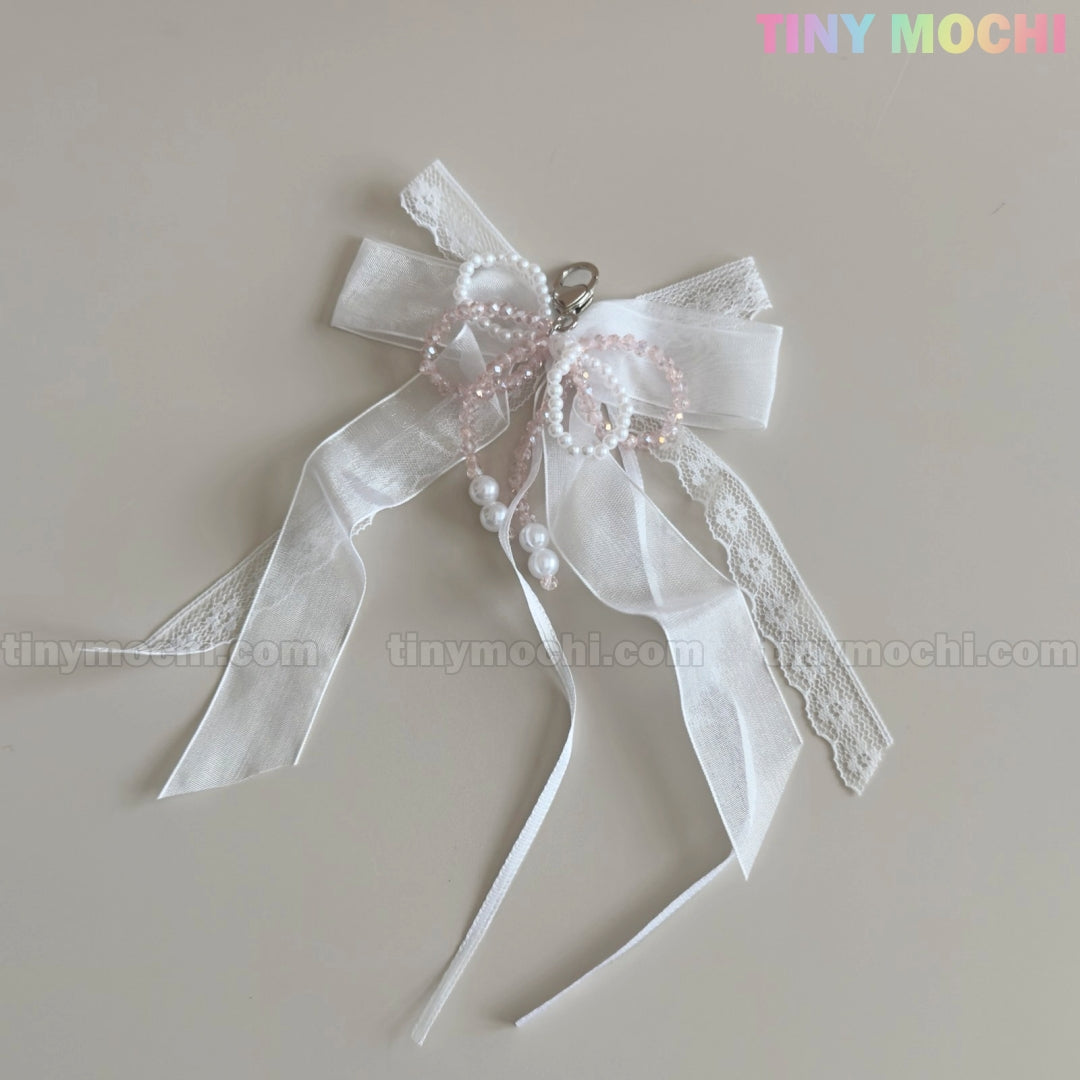 The Lace Bow Ribbon Keychain – Pearl Angelcore Bag Charm Clip by Tiny Mochi features delicate white lace, pearls, pink beads, cascading ribbons, and a metal clasp. “Tiny Mochi” appears in pastel at the top right. Perfect for keychains or angelcore style.