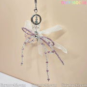 The Delicate Beaded Bow Charm – Elegant Y2K & Coquette Aesthetic Keychain from Tiny Mochi features a butterfly shape, purple and clear beads, and a sheer white ribbon bow, displayed against a light beige background.