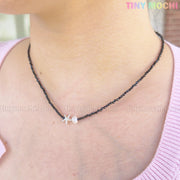 A person wearing the Tiny Mochi Sterling Silver Starfish Necklace—a handmade 925 silver charm on a black beaded pearl choker—styled with a light pink top.