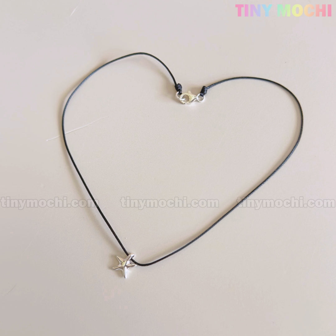 A Sterling Silver Starfish Necklace by Tiny Mochi, featuring a handmade 925 silver charm on a black beaded pearl choker, is shaped into a heart on a light background. The words TINYMICHI.COM and TINY MOCHI are faintly visible behind.