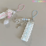 Two handmade Kawaii Pastel Lace Ribbon Keychain – Heart & Star Bag Charms by Tiny Mochi, one pink and white, one blue and white, with lace, ribbons, beads, and heart pendants are displayed on a light surface. Tiny Mochi logo at top right.