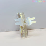 A kawaii hair claw clip shaped like a bunny with pancake and egg details rests open on a light surface. “Tiny Mochi” appears in pastel colors in the top right corner.