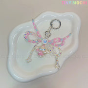 The Cotton Candy Wings Charm Keychain by Tiny Mochi features pink, blue, and clear pastel beads, a bow, and a small bear charm in kawaii fairycore style. Finished with a metallic clasp, it’s a cute phone or bag accessory.