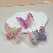 Three pastel NEW UV Color-Changing Butterfly Hair Claw Clips—Double Layer Acetate from Tiny Mochi rest on a white dish. Perfect for a Fairycore Aesthetic, the Tiny Mochi logo is in the top right corner.