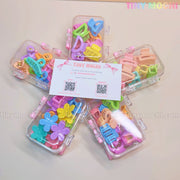 Five clear boxes, each holding the Tiny Mochi Kids Hair Clips Set with 10 colorful kawaii claw clips in butterfly, flower & heart designs, are arranged in a star around a Tiny Mochi card. The cute, kid-safe clips come in pastel shades.