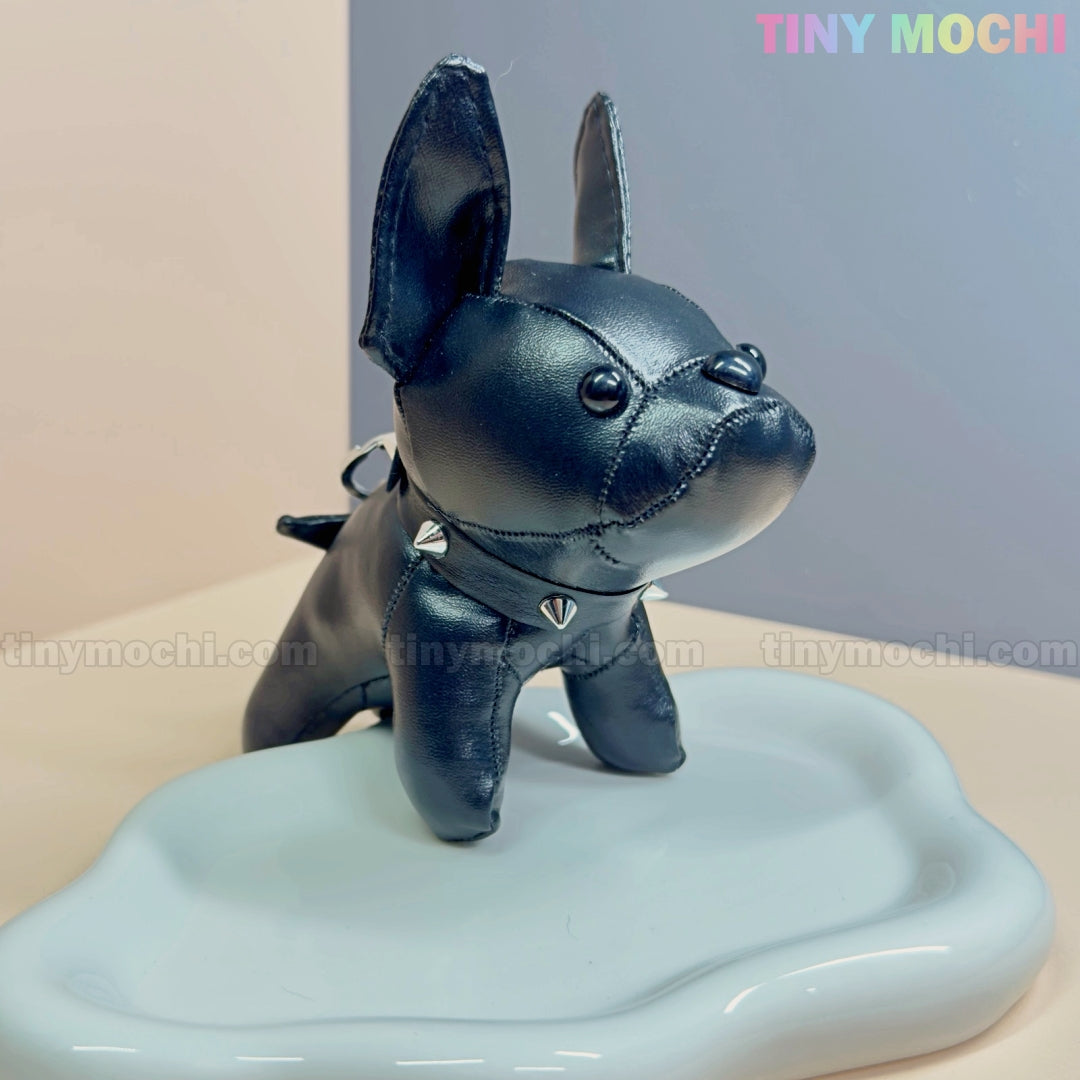 A cute black French Bulldog Keychain Coin Purse from Tiny Mochi, made of faux leather with a spiked collar, stands on a wavy white platform. “Tiny Mochi” in pastel colors appears at the top right—perfect gift for dog lovers!.