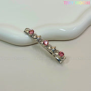 A silver hair clip with three pink gems and two silver stars rests on a cream ceramic dish. Ideal for Kawaii Gem Hair Clips for Girls by Tiny Mochi, these sparkly Y2K pins add Coquette flair. Tiny Mochi appears in rainbow text at the top right corner.
