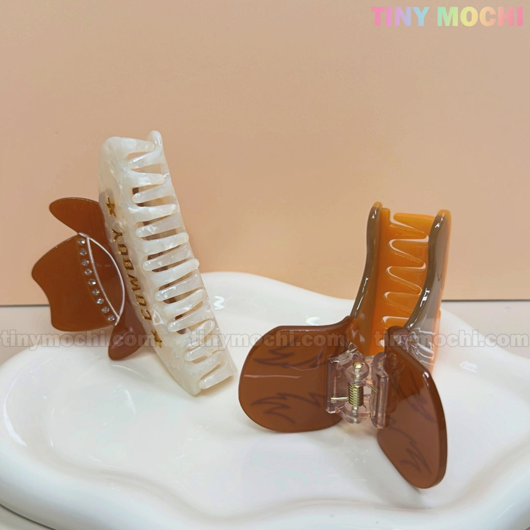 Tiny Mochi’s Western Cowboy Hair Claw Clips—cute cowgirl barrettes with boot and hat designs—are perfect Western hair accessories for women and girls, displayed upright on a white plate against a peach background.