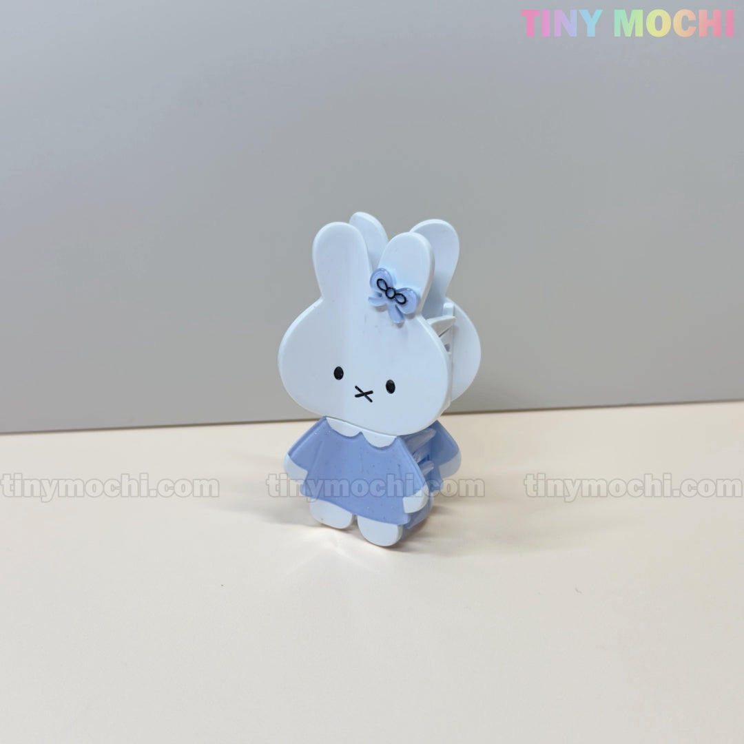 A cute pastel acrylic bunny hair claw clip, dressed in blue with a bow, stands on a light surface. The background is plain and the Tiny Mochi logo appears in the top right. Perfect for fans of the Kawaii Bunny Hair Claw Clip by Tiny Mochi.