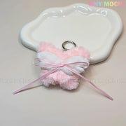 A Plush Butterfly Bow Keychain in pink from Tiny Mochi sits on a white, cloud-shaped dish. This fuzzy bag charm is a cute, coquette-inspired purse accessory—perfect for fans of kawaii gifts.
