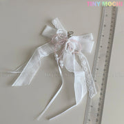 The Tiny Mochi Lace Bow Ribbon Keychain – Pearl Angelcore Bag Charm Clip, featuring white lace, pearls, and pink beads, is shown by a transparent ruler on a light surface. The pastel Tiny Mochi logo appears at the top right.