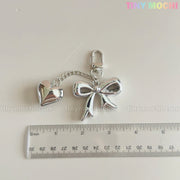 A Silver Bow Heart Keychain – Kawaii Mirror Bag Charm for Backpacks by Tiny Mochi is shown next to a ruler, measuring about 7 cm long. TINYMOSCHI.COM and Tiny Mochi are watermarked on the white background.
