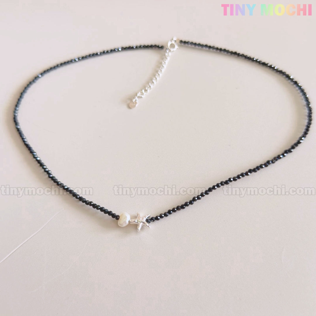 The Tiny Mochi Sterling Silver Starfish Necklace features a handmade 925 silver charm, black beaded choker with a freshwater pearl, and an adjustable clasp—an elegant coastal jewelry gift for her.