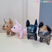 Four mini French Bulldog keychain coin purses by Tiny Mochi in brown, pink, black, and brown-black are lined up beside a clear ruler on a light surface. Cute faux leather puppy bag charms for dog lovers. Logo displayed at top right corner.