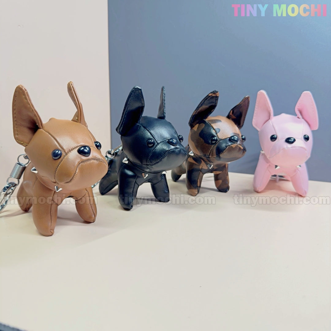 Four French Bulldog Keychain Coin Purse charms—brown, black, camouflage, and pink—are displayed in a row on a light surface. These cute faux leather zipper pouches by Tiny Mochi make perfect gifts for dog lovers.
