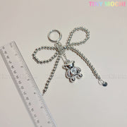 The Silver Teddy Bear Bow Keychain by Tiny Mochi, a cute bag charm accessory for women, teens, and kawaii lovers, hangs beside a clear ruler on a light surface. The branding TINY MOCHI and tinymochi.com are faintly visible.