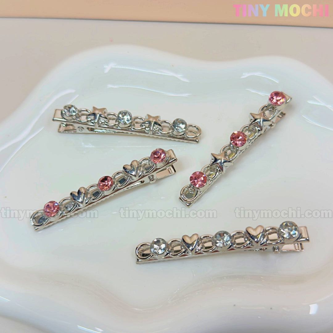 Four Kawaii Gem Hair Clips from Tiny Mochi rest on a white dish, featuring pink and blue gems with heart and star accents—perfect Coquette fashion. The Tiny Mochi logo appears in the top right.