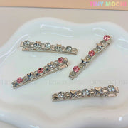 Four Kawaii Gem Hair Clips from Tiny Mochi rest on a white dish, featuring pink and blue gems with heart and star accents—perfect Coquette fashion. The Tiny Mochi logo appears in the top right.