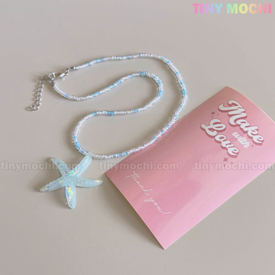 The Tiny Mochi Starfish Beach Necklace features an iridescent blue pendant choker beside a pink Make with Love & Thank you! card—handmade summer jewelry perfect for adding ocean aesthetic and mermaidcore vibes to any look.