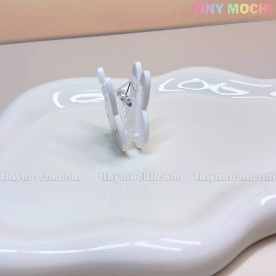 The Kawaii Bunny Paper Clip by Tiny Mochi—a cute Miffy-inspired binder clip—stands upright on a glossy white surface, perfect for desk decor. The beige background displays “Tiny Mochi” in pastel colors at the top right corner.