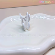 The Kawaii Bunny Paper Clip by Tiny Mochi—a cute Miffy-inspired binder clip—stands upright on a glossy white surface, perfect for desk decor. The beige background displays “Tiny Mochi” in pastel colors at the top right corner.