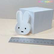 The Kawaii Bunny Face Hair Clip – White Rabbit Claw Clip by Tiny Mochi, featuring a cute bunny face design, is displayed before a white box and a centimeter ruler. Tiny Mochi appears in pastel colors at the top right.