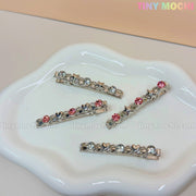 Four Tiny Mochi Kawaii Gem Hair Clips for Girls, each with sparkly rhinestones and heart or star accents, capture the Y2K coquette aesthetic on a white ceramic dish against a soft pastel background.