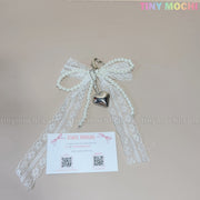 The Pearl Lace Bow Keychain with Silver Heart – Elegant Bag Charm by Tiny Mochi, featuring a coquette design, is displayed above a branded card with QR codes and social media—perfect as a chic accessory for your bag.