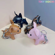 Four Tiny Mochi French Bulldog Keychain Coin Purses—mini faux leather dog bag charms in black, brown, pink, and camo with metallic spikes—are displayed. Cute puppy zipper pouch gifts for dog lovers!.