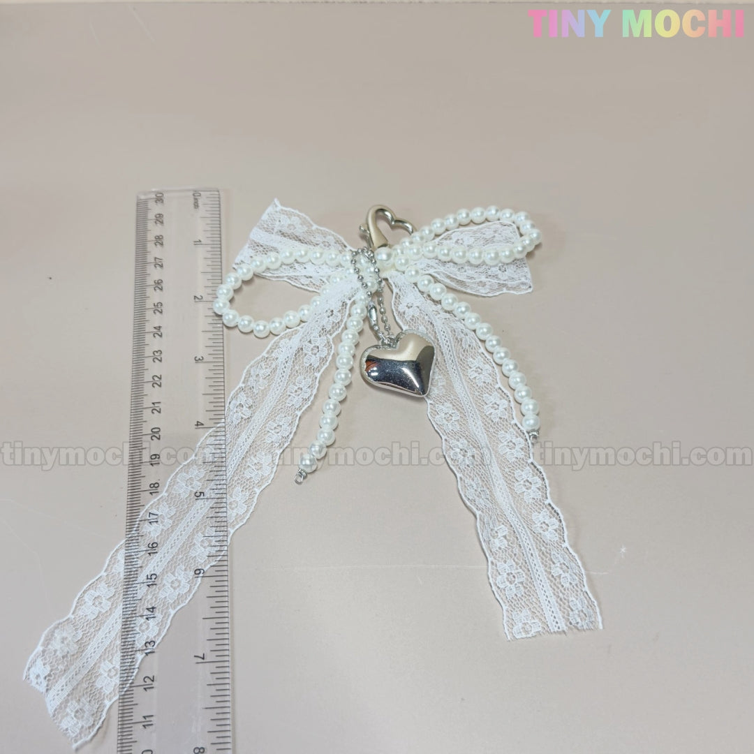 The Tiny Mochi Pearl Lace Bow Keychain with Silver Heart – Elegant Bag Charm, featuring pearl strands and a coquette aesthetic, lies beside a transparent 15 cm ruler on a light surface. The watermark TINY MOCHI appears in the image corners.