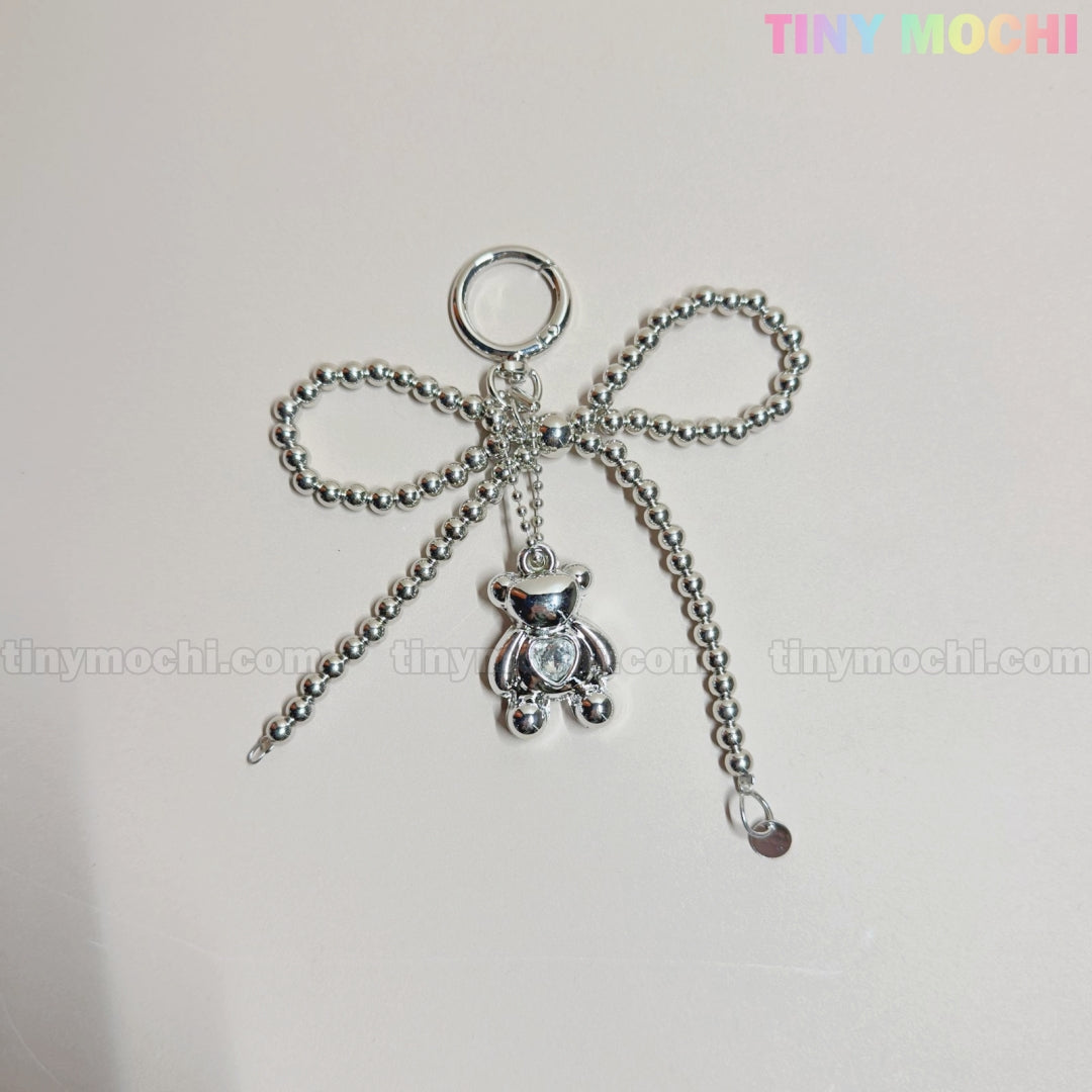 The Silver Teddy Bear Bow Keychain by Tiny Mochi, a cute bag charm for women and kawaii lovers, features silver beads and a dangling teddy bear. Displayed on a light background with tiny mochi in pastel at the top right.