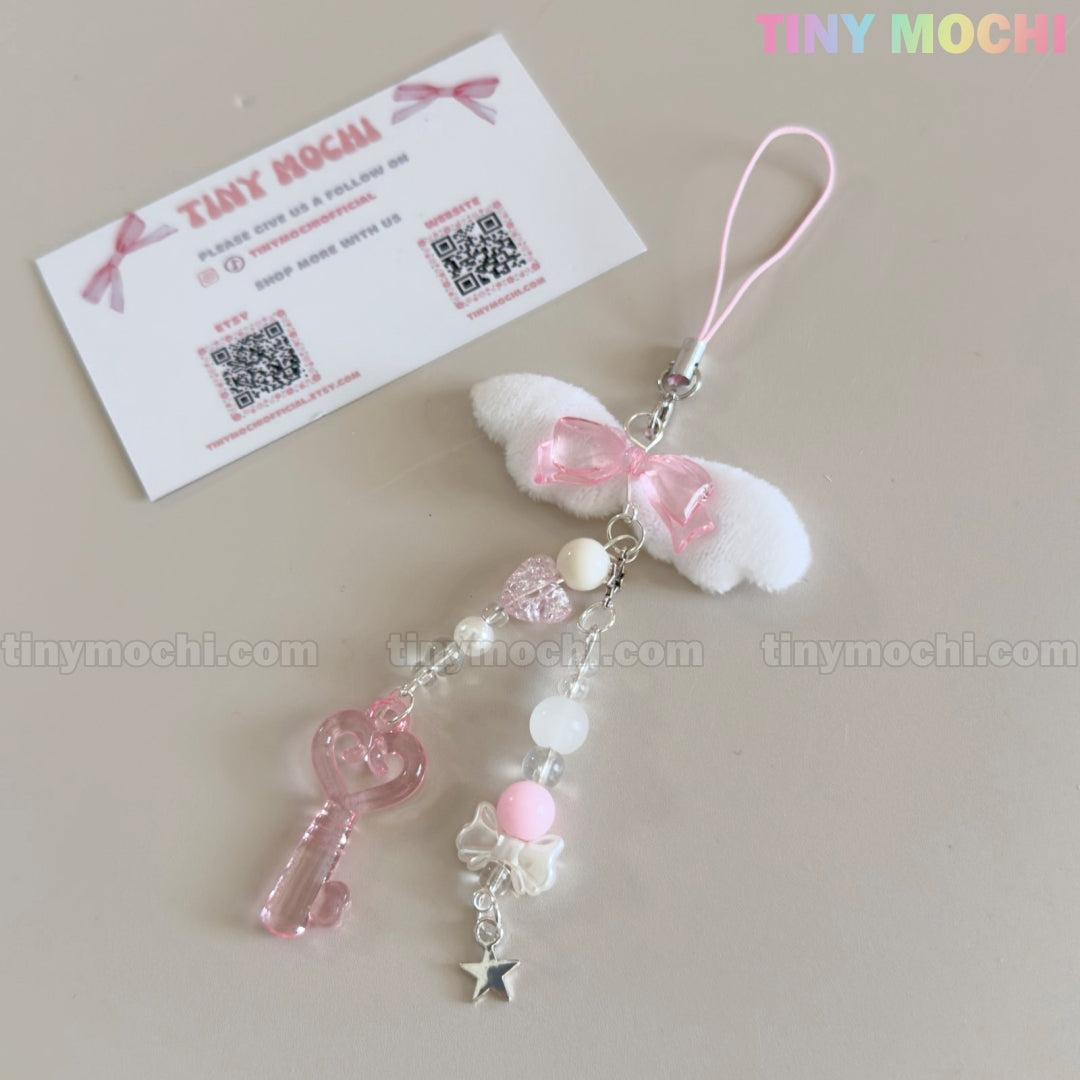 The Kawaii Angel Wing Keychain by Tiny Mochi features a pink heart charm, beads, white bow, and silver star accent—ideal for soft girl accessories. A Tiny Mochi business card with QR codes is in the softly styled, minimalist image background.