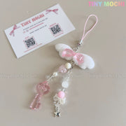 The Kawaii Angel Wing Keychain by Tiny Mochi features a pink heart charm, beads, white bow, and silver star accent—ideal for soft girl accessories. A Tiny Mochi business card with QR codes is in the softly styled, minimalist image background.