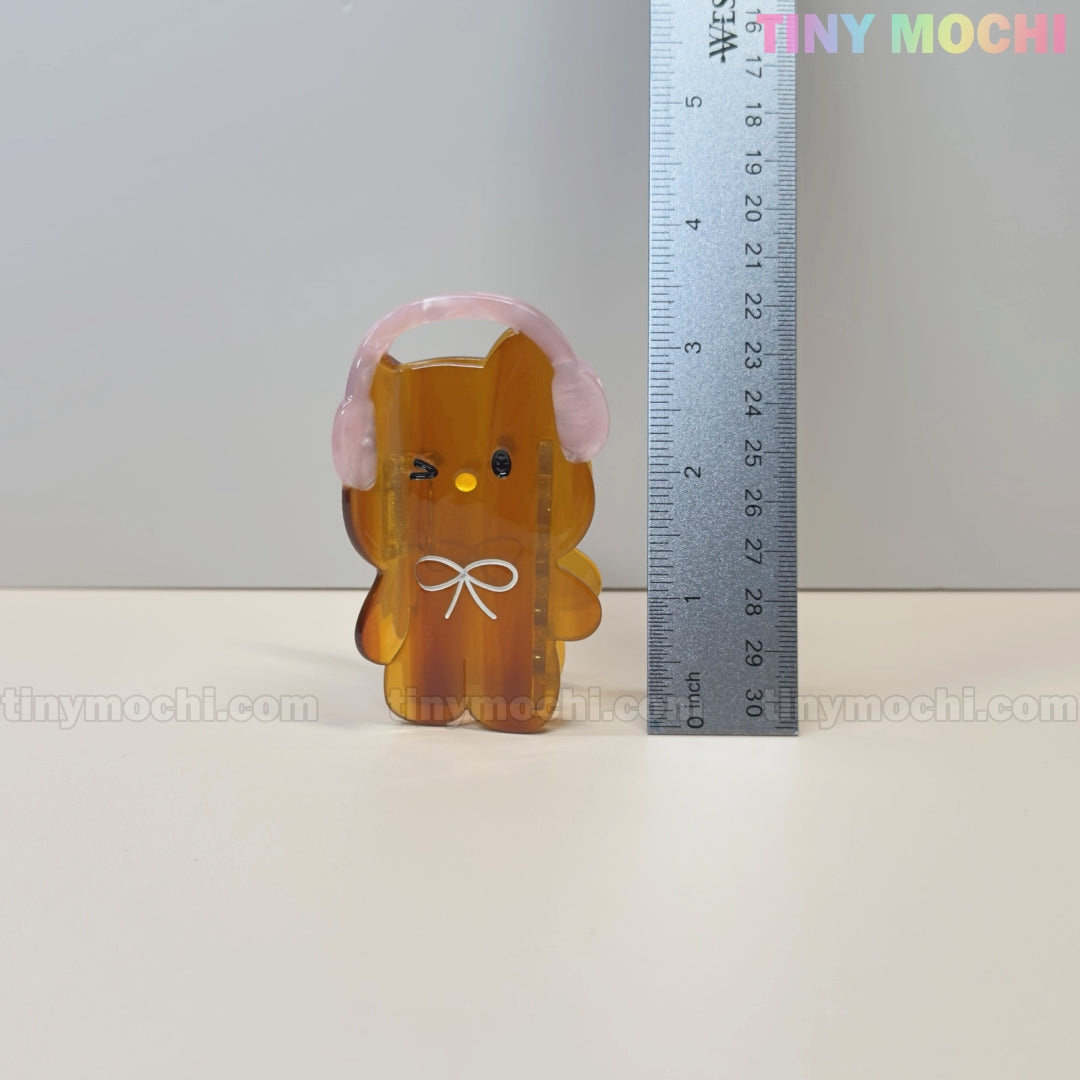 A cute amber bear hair claw clip with pink headphones and a white bow stands beside a 7 cm ruler. Tiny Mochi is displayed on the plain background—a kawaii accessory from the Kawaii Bunny & Bear Hair Claw Clips collection.