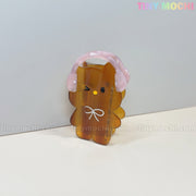 A cute brown bear-shaped Kawaii Bunny & Bear Hair Claw Clip with pink headphones and a white bow stands on a white surface; TINY MOCHI is displayed in pastel colors at the top right.