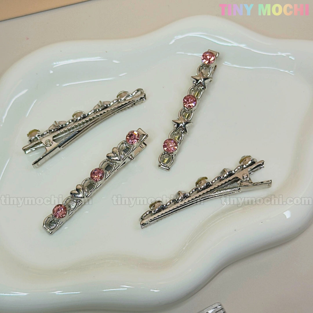 Four Kawaii Gem Hair Clips for Girls by Tiny Mochi, featuring pink gems and star accents, are shown on a white dish. Tiny Mochi appears in pastel colors at the top right against a neutral background, evoking sparkly Y2K vibes.