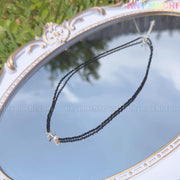 The Tiny Mochi Sterling Silver Starfish Necklace features a handmade 925 silver starfish charm and freshwater pearl on a black beaded choker, shown outdoors on a white and gold mirror reflecting sky and greenery.