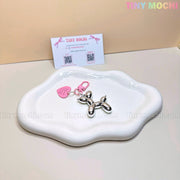 A Chrome Silver Balloon Dog Keychain with a pink heart tag from Tiny Mochi adds Y2K flair as it sits on a wavy white ceramic dish, with a Tiny Mochi business card displayed upright in the background.