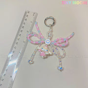 The Cotton Candy Wings Charm Keychain by Tiny Mochi, a kawaii beaded fairycore accessory with a bow, is shown beside a clear ruler on a light background. Tiny Mochi appears in pastel colors at the top right.