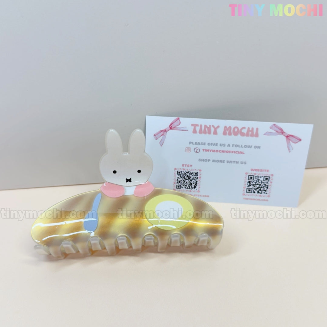 The Kawaii Bunny Breakfast Hair Claw Clip by Tiny Mochi, featuring a cute pancake and egg design, is displayed on a white surface in front of a pastel Tiny Mochi business card with pink bows.