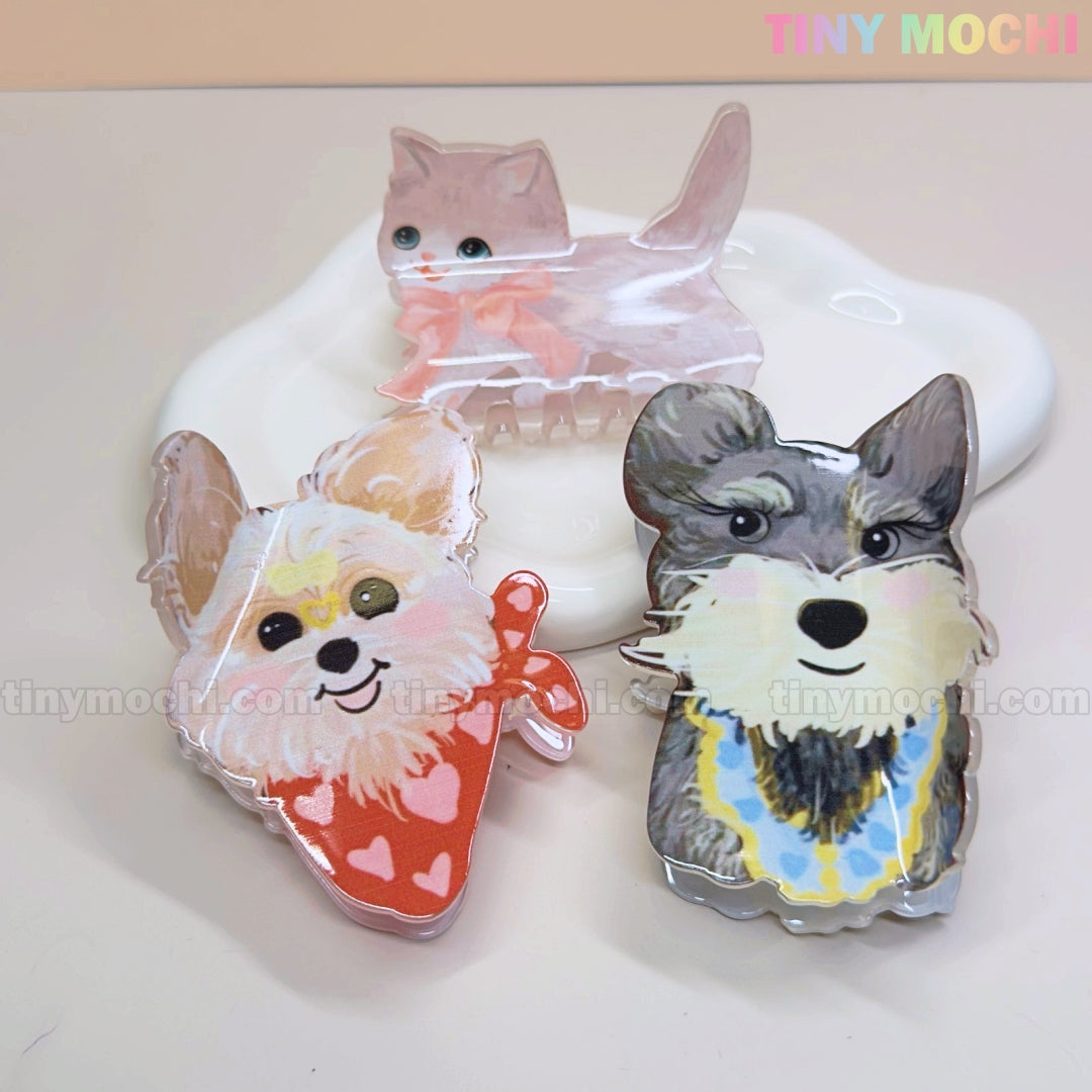 Three Tiny Mochi Kawaii Dog & Cat Hair Claw Clips—featuring a gray cat, cream dog, and gray dog in cute accessories—sit on a white dish. Adorable cartoon pet animal claws to add charm to any look for girls.