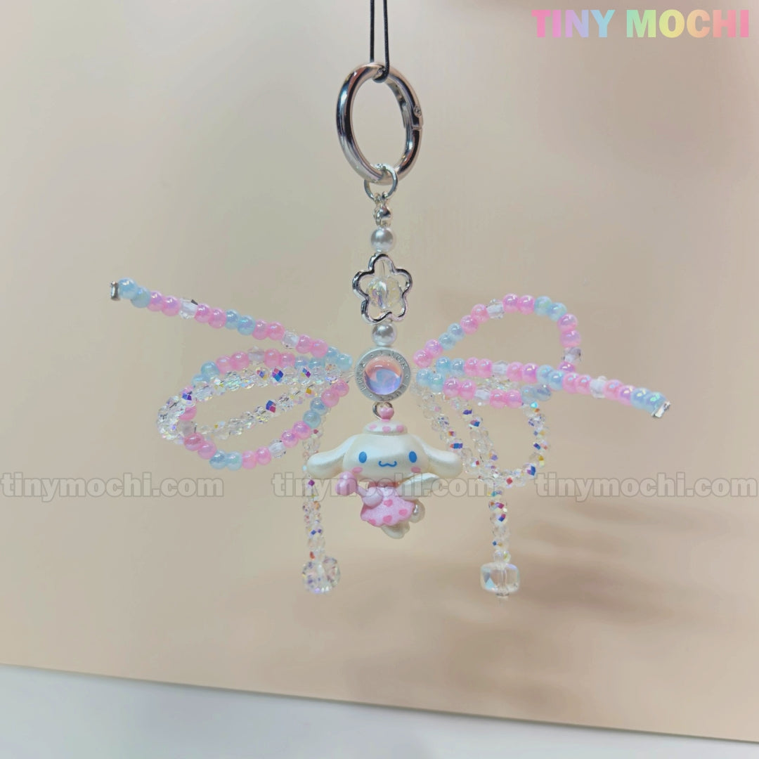 The Cotton Candy Wings Charm Keychain by Tiny Mochi features pastel pink, blue, and purple wings, a cute white character with a pink heart, and beaded bow details—perfect as a kawaii fairycore phone charm or gift accessory.