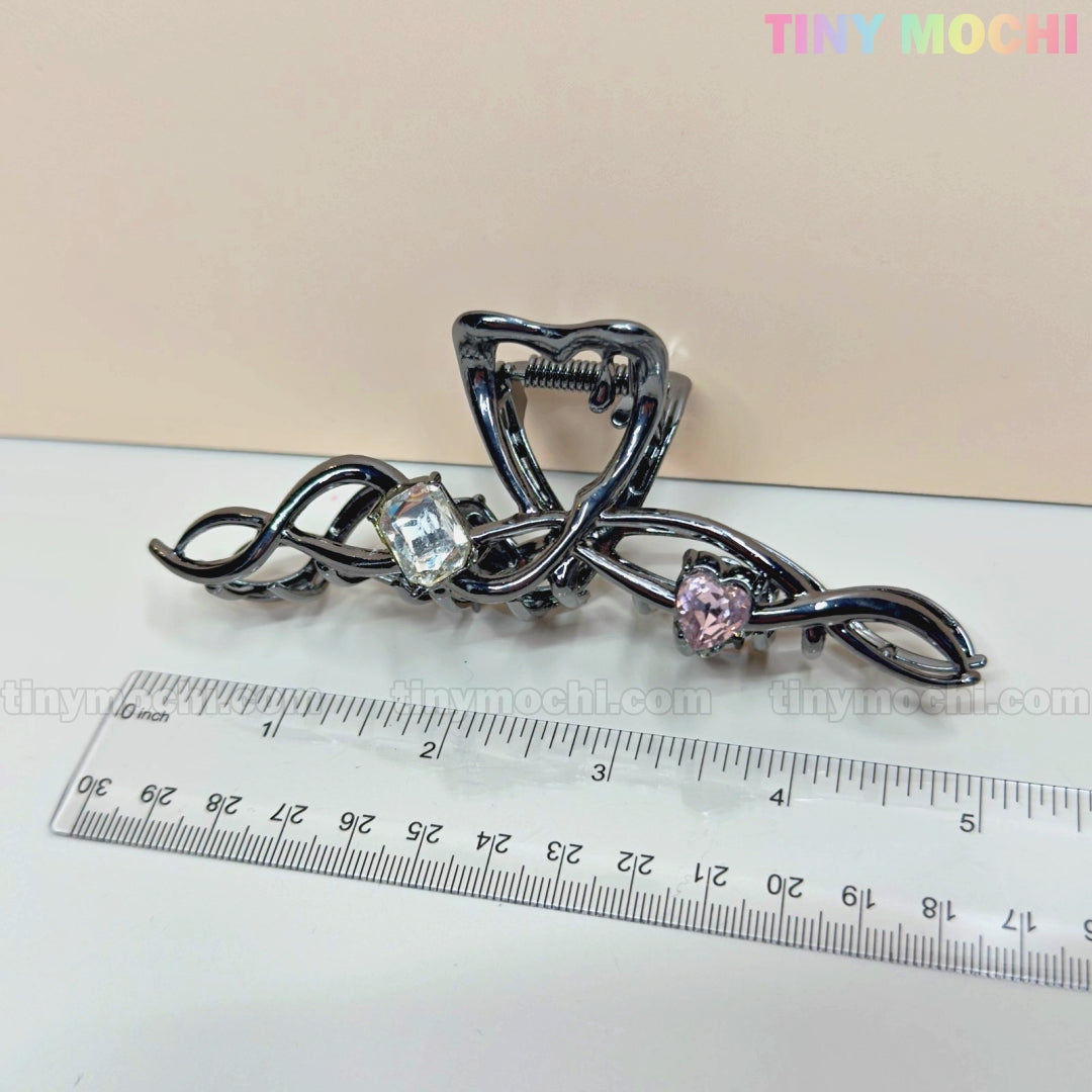The Dark Silver Crystal Heart Hair Claw by Tiny Mochi, an elegant metal hair clip for women with a wavy design and crystal heart accent, is shown next to a clear ruler on a light surface. The Tiny Mochi brand name appears in the top right.
