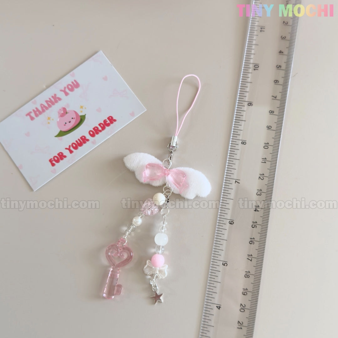 A pink and white beaded phone charm with bow, key, bear, and star lies by a 15 cm ruler and a peach-themed Thank You card—perfect for pairing with your Tiny Mochi Kawaii Angel Wing Keychain – Pink Heart Charm Bag Accessory.