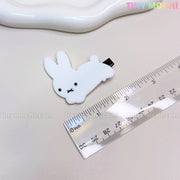 A small, white bunny from the “Kawaii Bunny and Bear Hair Clips for Girls” by Tiny Mochi rests next to a ruler on a beige surface. The clip features black eyes, an “X” mouth, and the Tiny Mochi logo appears in the top right corner.