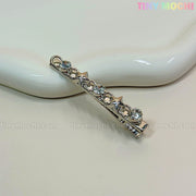 A silver Kawaii Gem Hair Clip from Tiny Mochi, featuring star shapes and rhinestones, sits on a white wavy dish. Perfect for Y2K and coquette styles, Tiny Mochi appears in colorful letters at the top right.