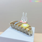 The Kawaii Bunny Breakfast Hair Claw Clip by Tiny Mochi features a cute bunny with pancakes and eggs, displayed on a white and beige background as an adorable acrylic hair accessory for women and girls.