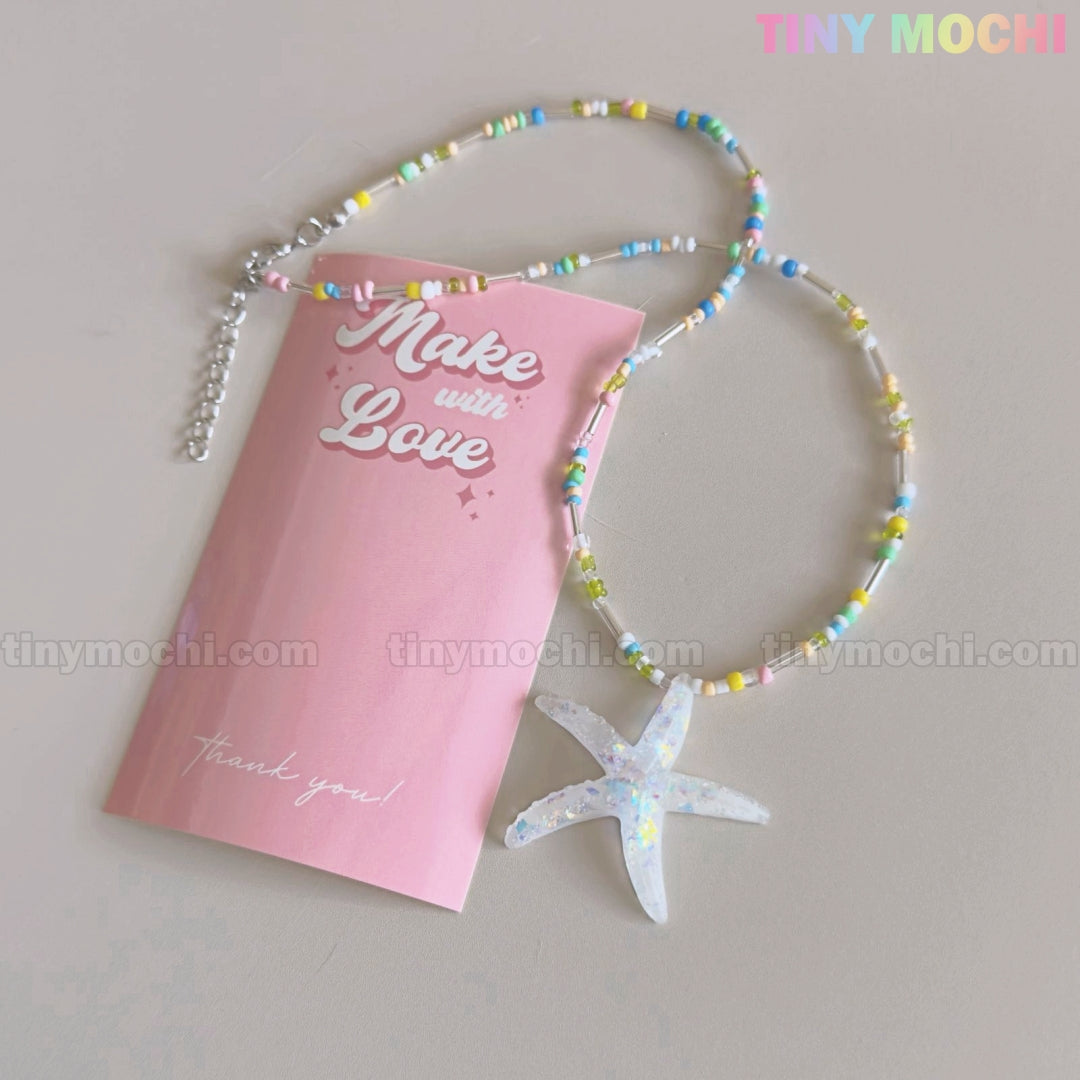 The Pastel Starfish Beach Bead Necklace by Tiny Mochi features a handmade iridescent resin pendant on a pink card reading Make with Love. This kawaii oceancore choker, perfect for girls and teens, rests on a light background.
