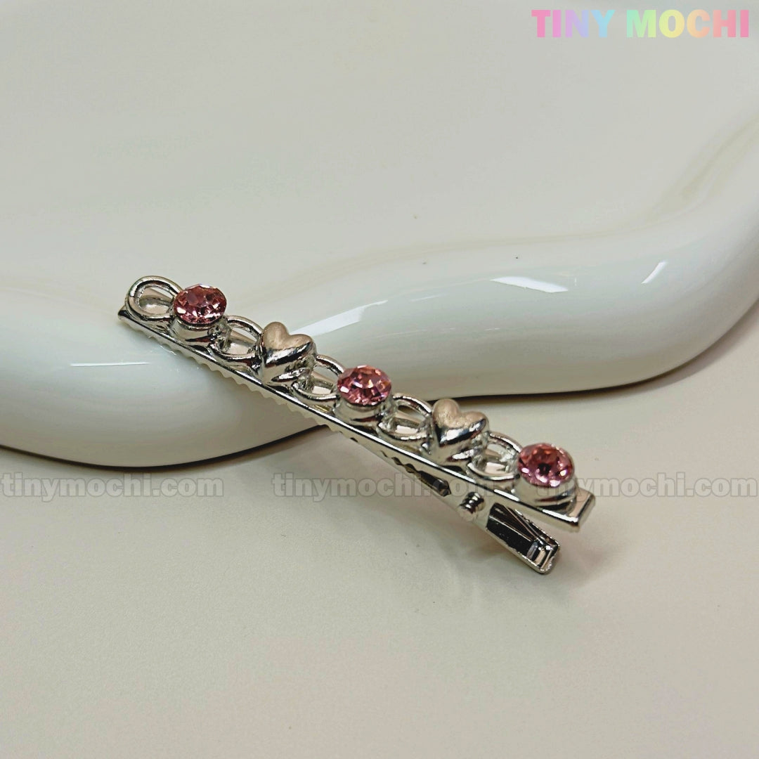 The Tiny Mochi Kawaii Gem Hair Clips for Girls feature silver pins adorned with alternating pink rhinestones and small silver hearts—perfect sparkle for Y2K lovers and Coquette aesthetic fans. Product shown on a white ceramic dish with the tinymochi.com watermark.