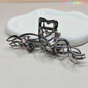 The Dark Silver Crystal Heart Hair Claw by Tiny Mochi, an elegant metal hair clip featuring pink and clear crystal heart accents, is displayed in front of a white dish. Tiny Mochi appears in pastel at the top right.
